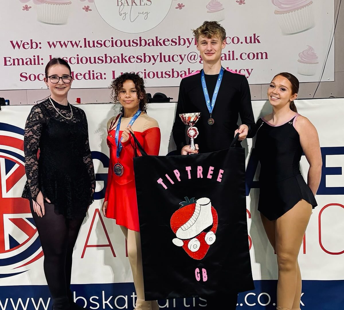 Four TARSC skaters in costume holding a Tiptree GB flag after competing internationally.