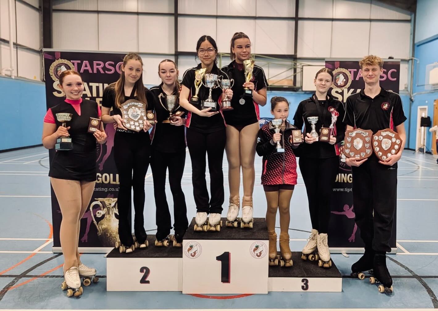 TARSC skaters on the podium holding trophies and shields at the club's annual Merit Competition.