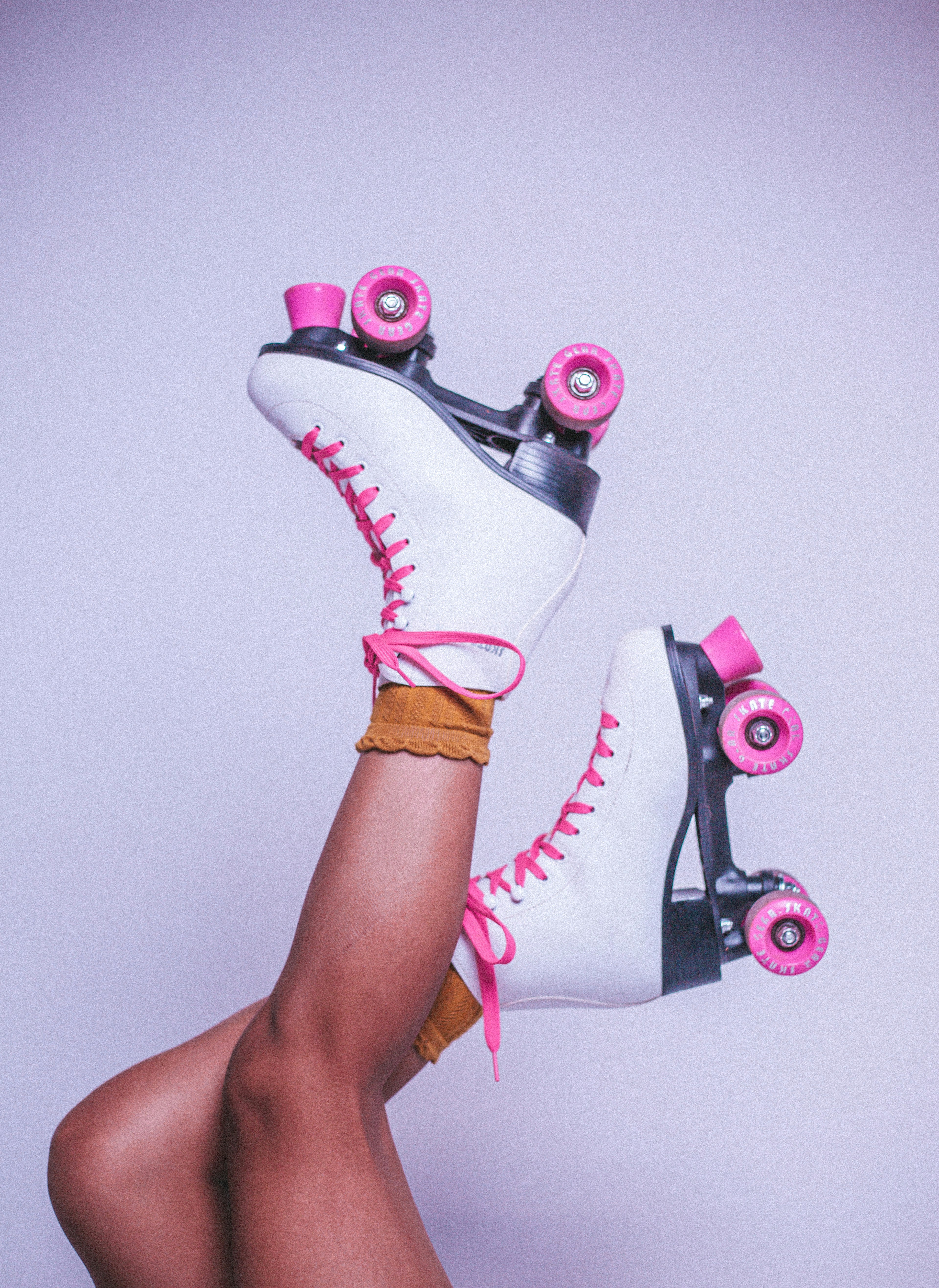 A pair of white quad roller skates with pink laces and pink wheels.